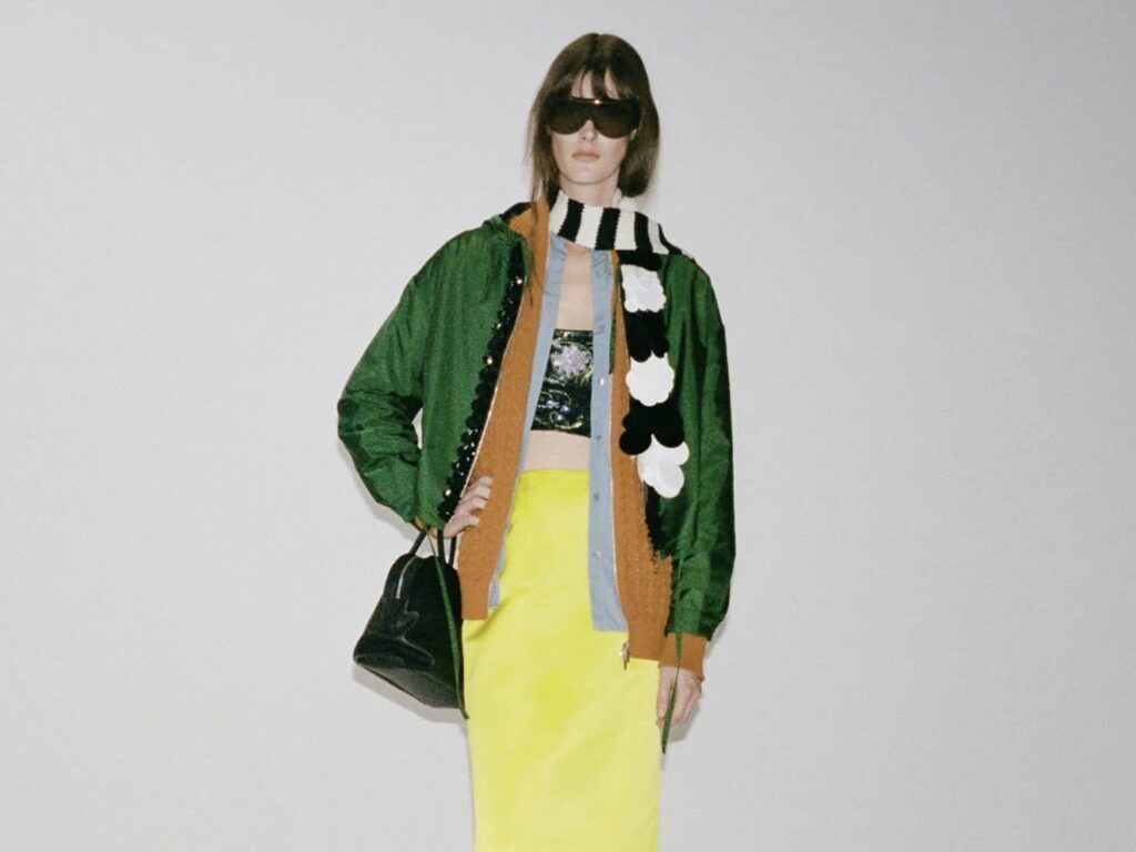 Model trägt einen neongelben Pencil Skirt mit farbenfrohen Layers, grüner Jacke und gestreiftem Schal