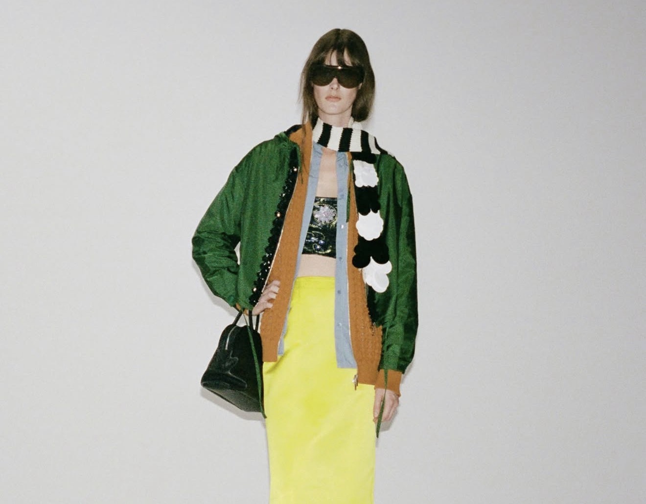 Model trägt einen neongelben Pencil Skirt mit farbenfrohen Layers, grüner Jacke und gestreiftem Schal