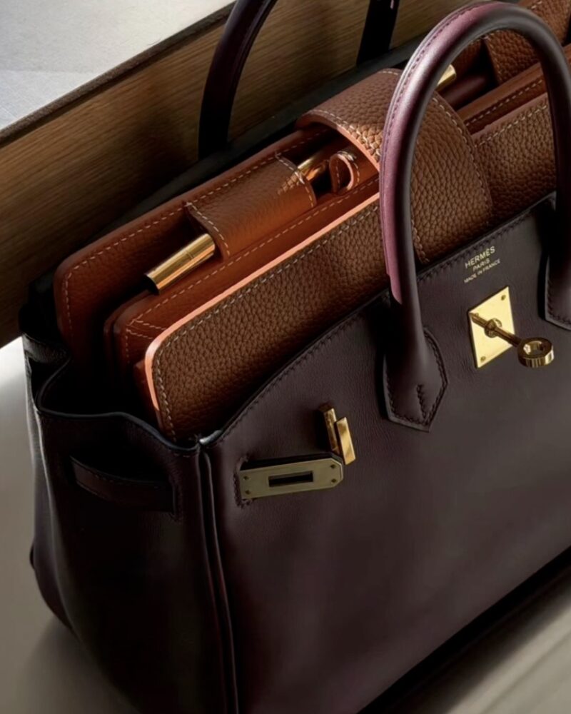 Nahaufnahme eines braunen Agende-Lederplaners mit goldenem Stift in einer dunkelvioletten Handtasche.